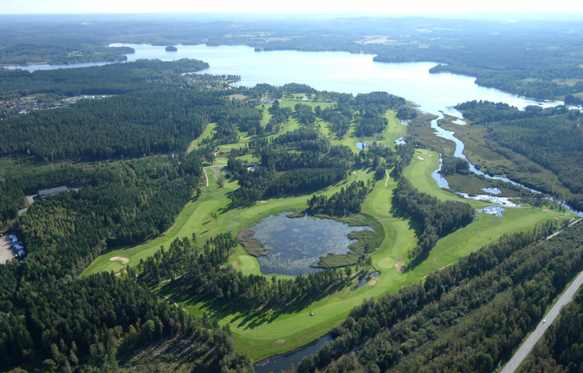 Flygbild över golfbana med damm, fairways och sjö i bakgrunden